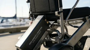 Close-up photorealistic illustration of the 'LONG-RANGE POWER' high-capacity lithium-ion battery pack being inserted into a lightweight electric wheelchair.