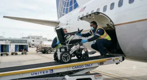 Ground crew carefully loading an airline approved power wheelchair into the cargo hold of a commercial airplane